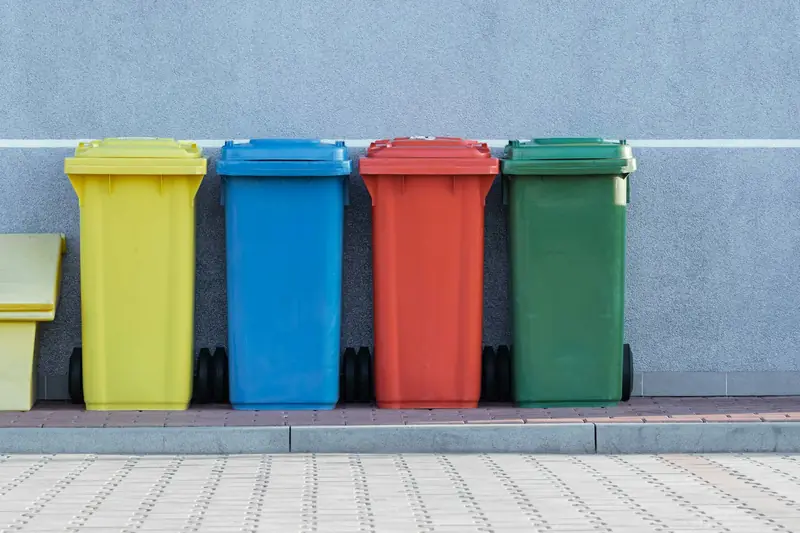 Coloured recycling bins lined up against a wall